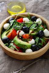 Green Avocado Salad with cherry tomatoes, olive, mozzarella and arugula closeup