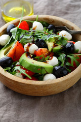 Avocado Salad with cherry tomatoes, olive, mozzarella and arugula closeup