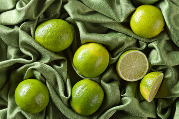 Group of whole and cut fresh limes on green satin