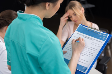 internist filling medical form while patient sitting behind in clinic