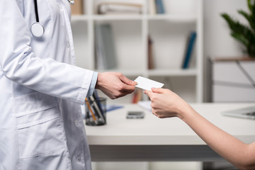 partial view of doctor giving blank card to patient at clinic