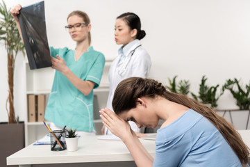 Fototapeta premium upset patient sitting at hospital while focused doctors looking at x-ray picture together