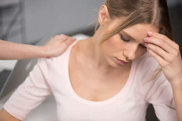 Obraz premium Cropped shot of person supporting upset young woman sitting with hand on forehead and thinking