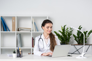 young caucasian doctor working and typing in laptop while sitting at table in clinic