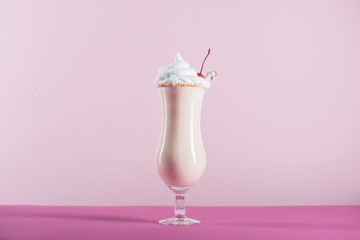 fresh milkshake with cream and cherry on top in glass on pink tabletop
