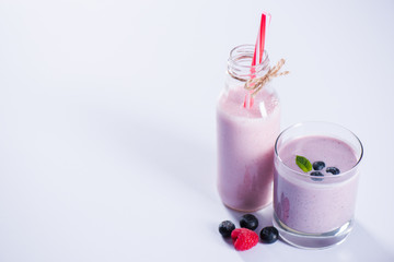 close up of smoothie with blueberries in glass and bottle with drinking straw