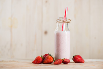 sweet milkshake with straw in bottle and fresh strawberries on tabletop