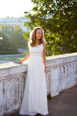 Elegant bride in a white dress near to white old concrete fence