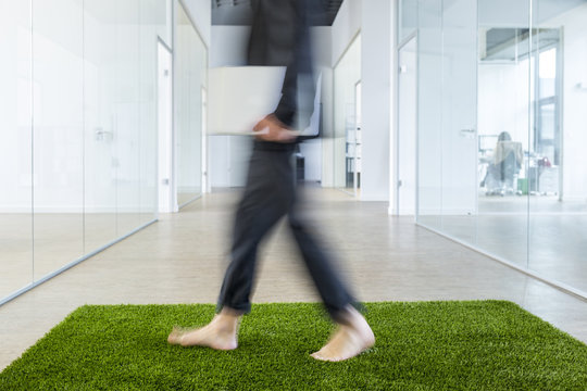 Mature businessman walking barefoot on grass carpet in office - Powered by Adobe