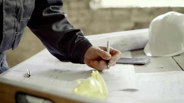 The male engineer is making adjustments to the construction site drawings, he is in the building of the former factory, which will be modernized