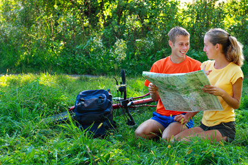 Young couple tourist with map in hand sitting on the grass