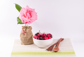 Cherries in white bowl and wooden spoon  with flowers on white background