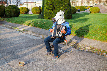 Man with a horse head street musician playing the accordion outdoors, funny prank