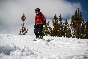 Fototapeta na wymiar Teenage Boy snowboarding down steep snowy hill in the mountains