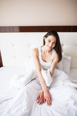 Beautiful young smiling woman sitting on bed and stretching in the morning at bedroom.