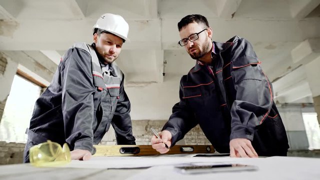 The architect and the superintendent with a helmet for protection on the head are discussing the possibility of making amendments to the building construction plan