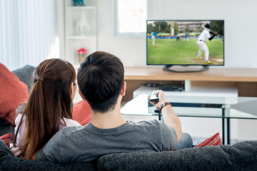 Naklejka premium Young Asian couple waching baseball sport on tv at home