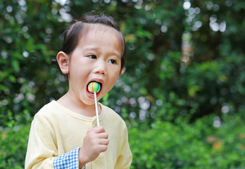 Little child girl enjoy eating lollipop candy in the park.