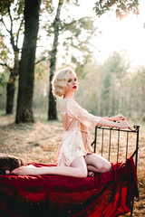 Beautiful and elegant blonde woman with red lips and hair waves wearing beige nightie posing on the...
