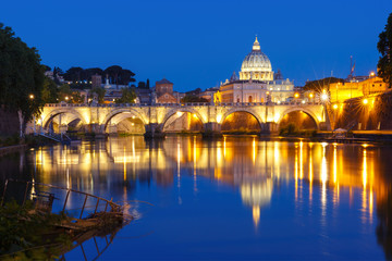 Saint Angel bridge and Saint Peter Cathedral with a mirror reflection in the Tiber River during morning blue hour in Rome, Italy.