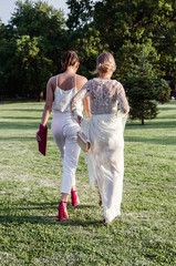 Naklejka na ściany i meble two elegant women with their backs walking through the park on the grass