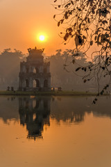 Sun rising behind the Turtle Tower in the center of Hoan Kiem Lake (Lake of the Returned Sword)....