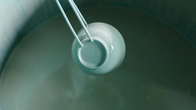 Ceramic artisan in Caltagirone submerging a bowl into enamel