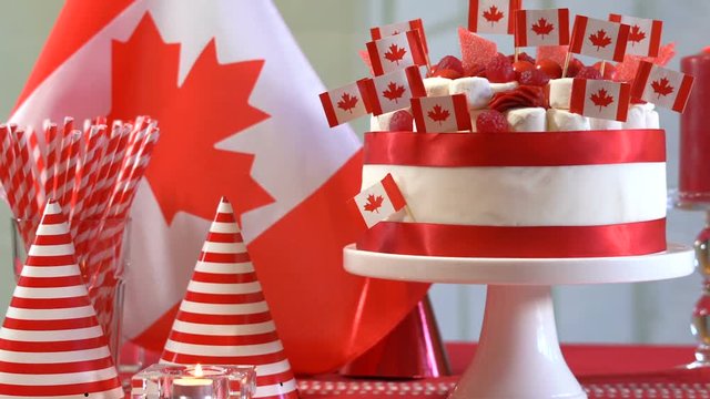 Happy Canada Day party table with red and white cake decorated with maple leaf red Canadian Flags, marshmallows and candy, dolly slider shot.