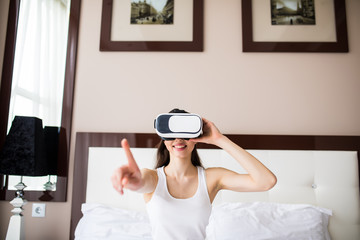 Young woman lying on bed, using Vr Glasses at home