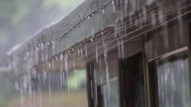 Rain drops falling from roof's eave during rain storm