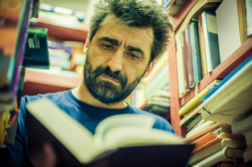 Curious man reading book between the shelves in the library