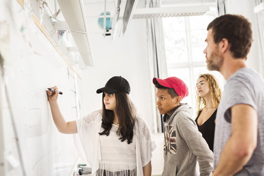 Student (14-15) writing on whiteboard, teacher looking