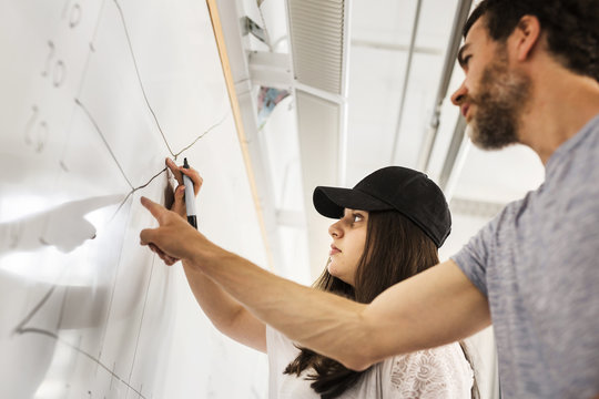 Student (14-15) writing on whiteboard, teacher looking