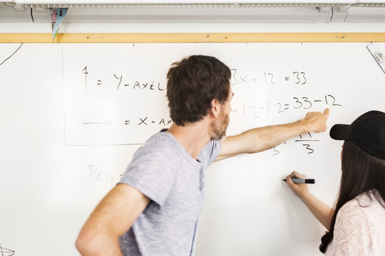 Student (14-15) writing on whiteboard, teacher looking