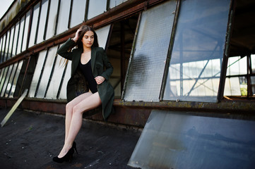 Sexy model girl wit long legs at black lingerie outfit body swimsuit combidress and jacket posed at the roof of abadoned industrial place with windows.