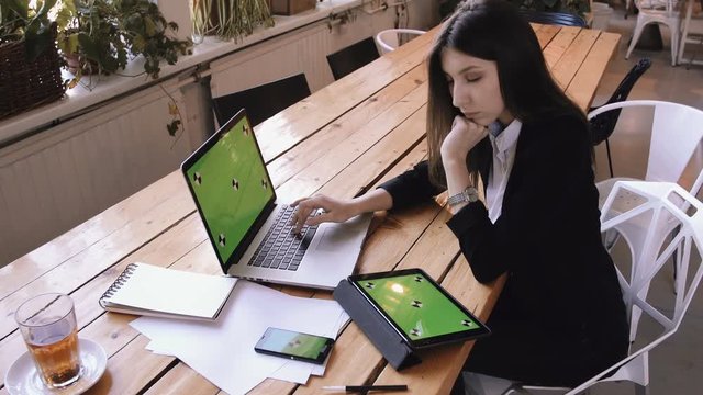 Businesswoman using tablet computer with green touch screen in cafe on wood table.