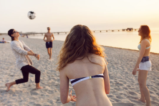 Young Men, Young Woman And Teenage Girl (16-17) Playing Volleyball On Sand At Sunset