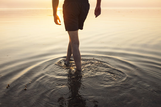 Man in shorts wading in sea at sunset