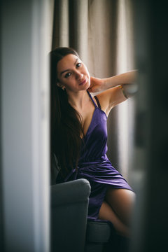 Sexy beautiful girl posing in a  room with violet dress, photographed in a paparazzi styl,spied style with foreground unfocused