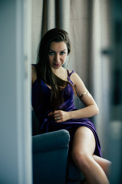 Sexy beautiful girl posing in a  room with violet dress, photographed in a paparazzi styl,spied style with foreground unfocused