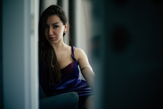 Sexy beautiful girl posing in a  room with violet dress, photographed in a paparazzi styl,spied style with foreground unfocused
