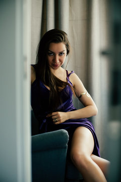 Sexy beautiful girl posing in a  room with violet dress, photographed in a paparazzi styl,spied style with foreground unfocused