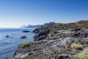 Fototapeta na wymiar Scogliera di roccia vulcanica con vista su Lipari e Salina sullo sfondo, isola di Vulcano - arcipelago delle Isole Eolie IT