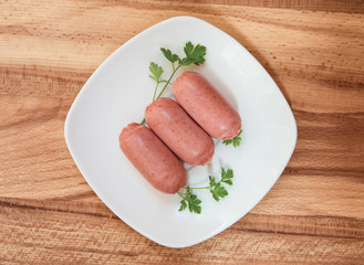 Breakfast cooked mini sausage with parsley on a white round plate on light wooden table top view