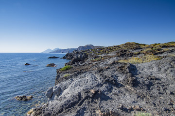 Fototapeta na wymiar Scogliera di roccia vulcanica con vista su Lipari e Salina sullo sfondo, isola di Vulcano - arcipelago delle Isole Eolie IT 