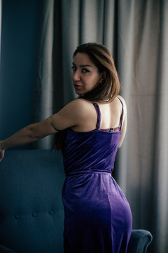 Sexy beautiful girl posing in a  room with violet dress, photographed in a paparazzi styl,spied style with foreground unfocused