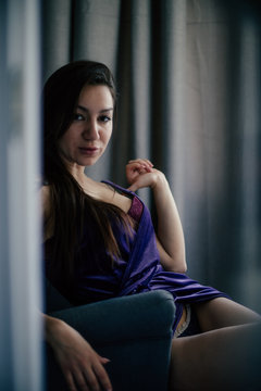 Sexy beautiful girl posing in a  room with violet dress, photographed in a paparazzi styl,spied style with foreground unfocused