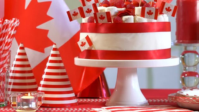 Happy Canada Day party table with red and white cake decorated with maple leaf red Canadian Flags, marshmallows and candy, panning across and up to cake.