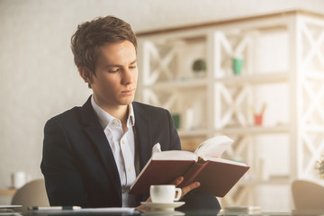 Attractive guy drinking coffee and reading book