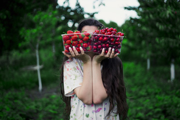 The girl holds two boxes filled with strawberries and cherries against the backdrop of the garden. Conception: choice food vegan